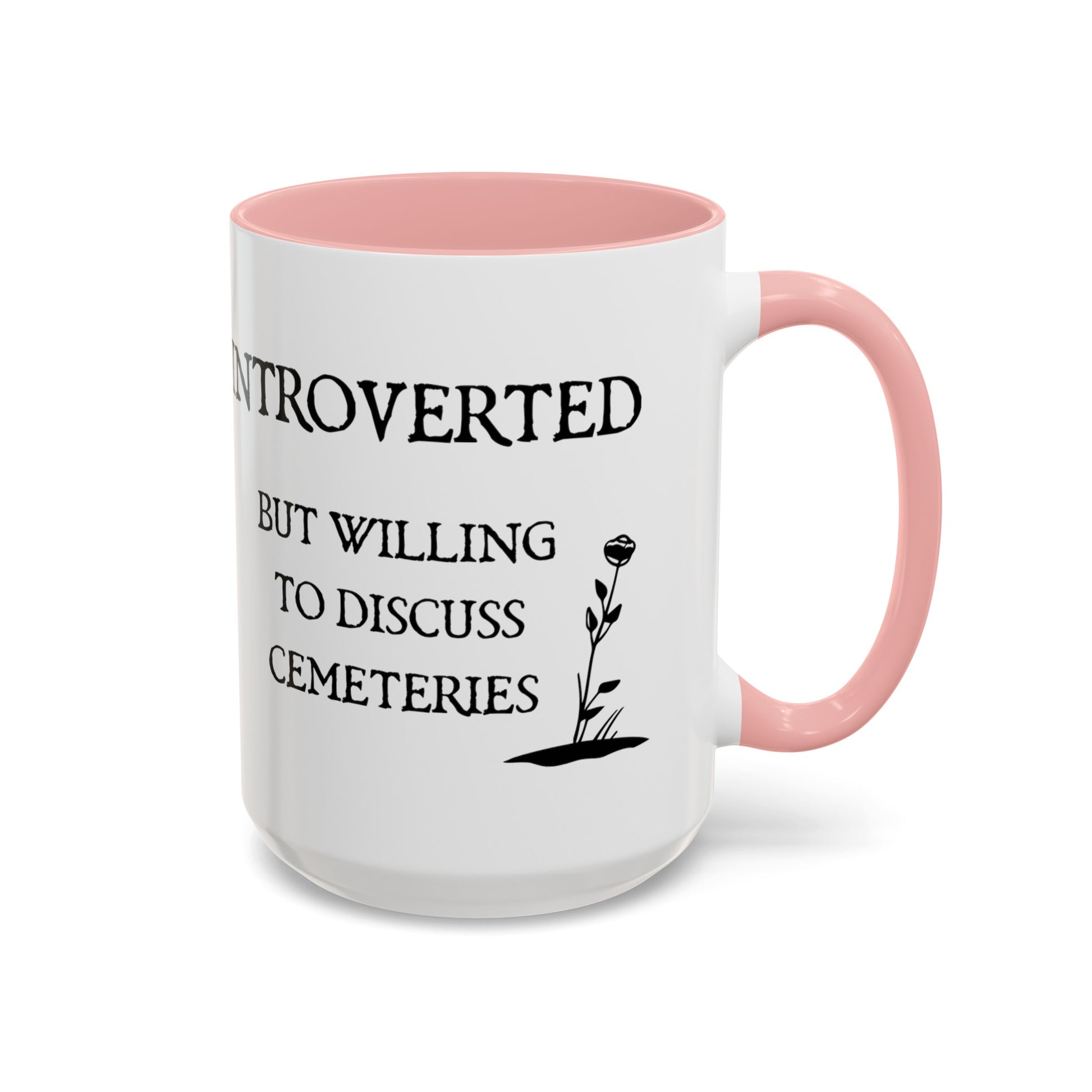 15 oz white ceramic mug with black text and graphics and  a pink handle and pink interior. One side says Introverted but willing to discuss cemeteries the other side has a tombstone with a skull on it