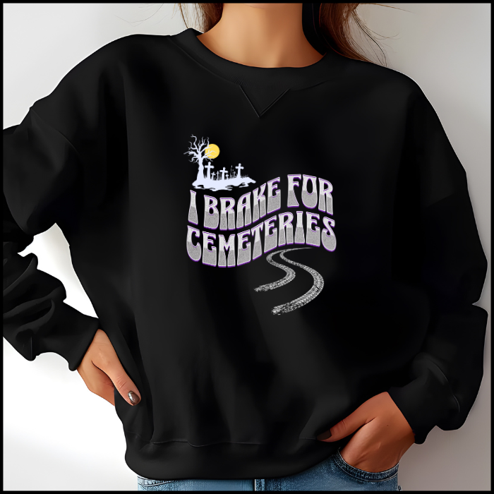 Gildan 18000 Crewneck Sweatshirt with the words I Brake For Cemeteries in medium and light grey with purples shading accents.. There are skid marks under the words and a small graveyard graphic to the top left of the words. The sweatshirt is black