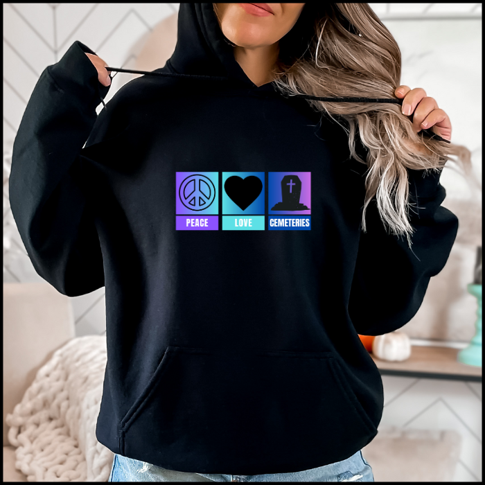 Gildan 18500 Hoodie Sweatshirt with the words peace, love, cemeteries across the chest with matching symbols, a peace sign, a heart and a tombstone on an ombre back ground of purple, aqua and blue. Hoodie color is black.