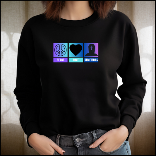 Bella Canvas 3501 long sleeve shirt with the words peace, love , cemeteries across the front with related symbols above the words. A round peace sign, a heart and a coffin. The back ground is ombre purple, aqua and blue. Shirt color is black.